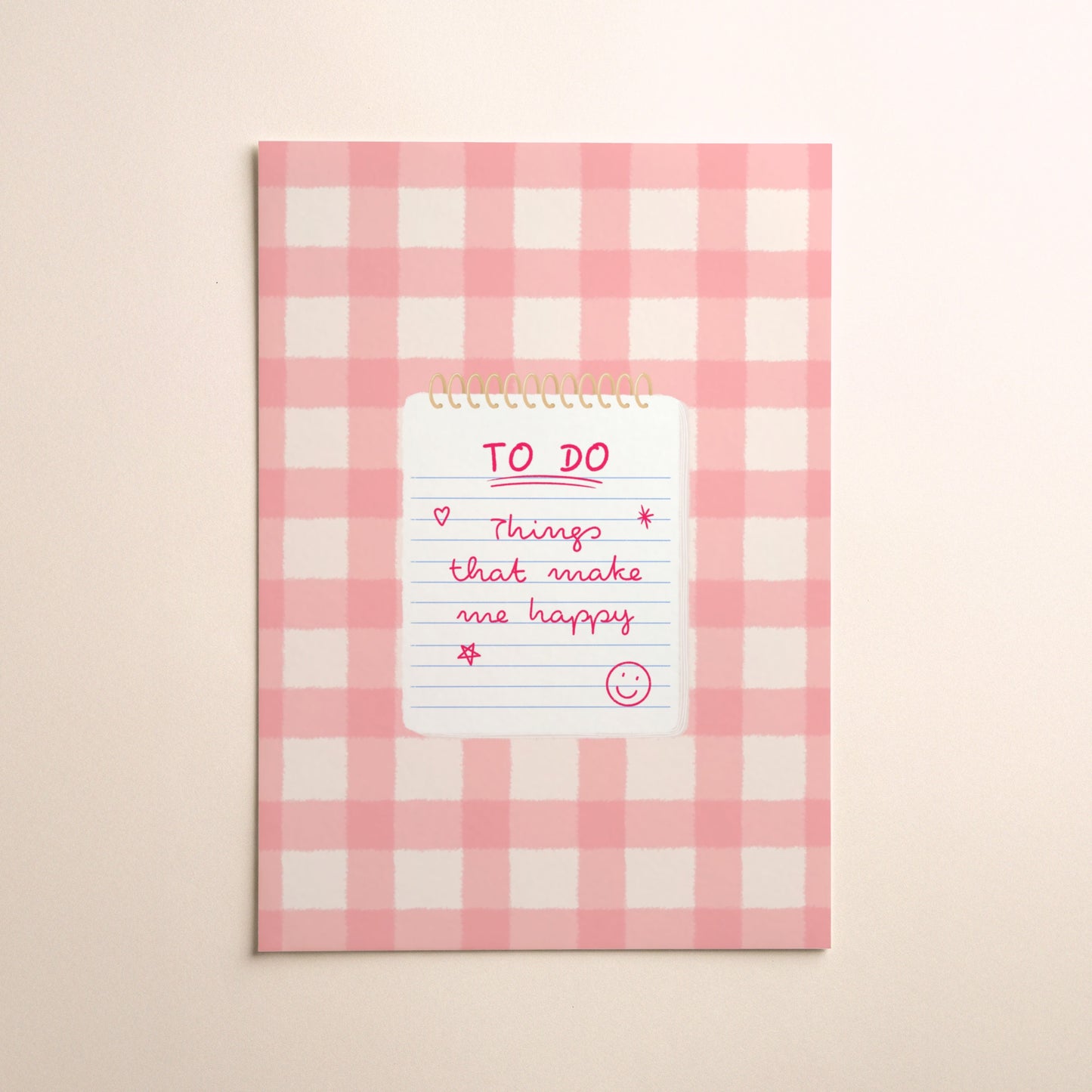 A pink and white gingham illustration print with a white notepad with gold spiral binding, featuring a pink handwritten 'TO DO' list that says ‘Things that make me happy’ with a smiley face, set against a warm beige background.