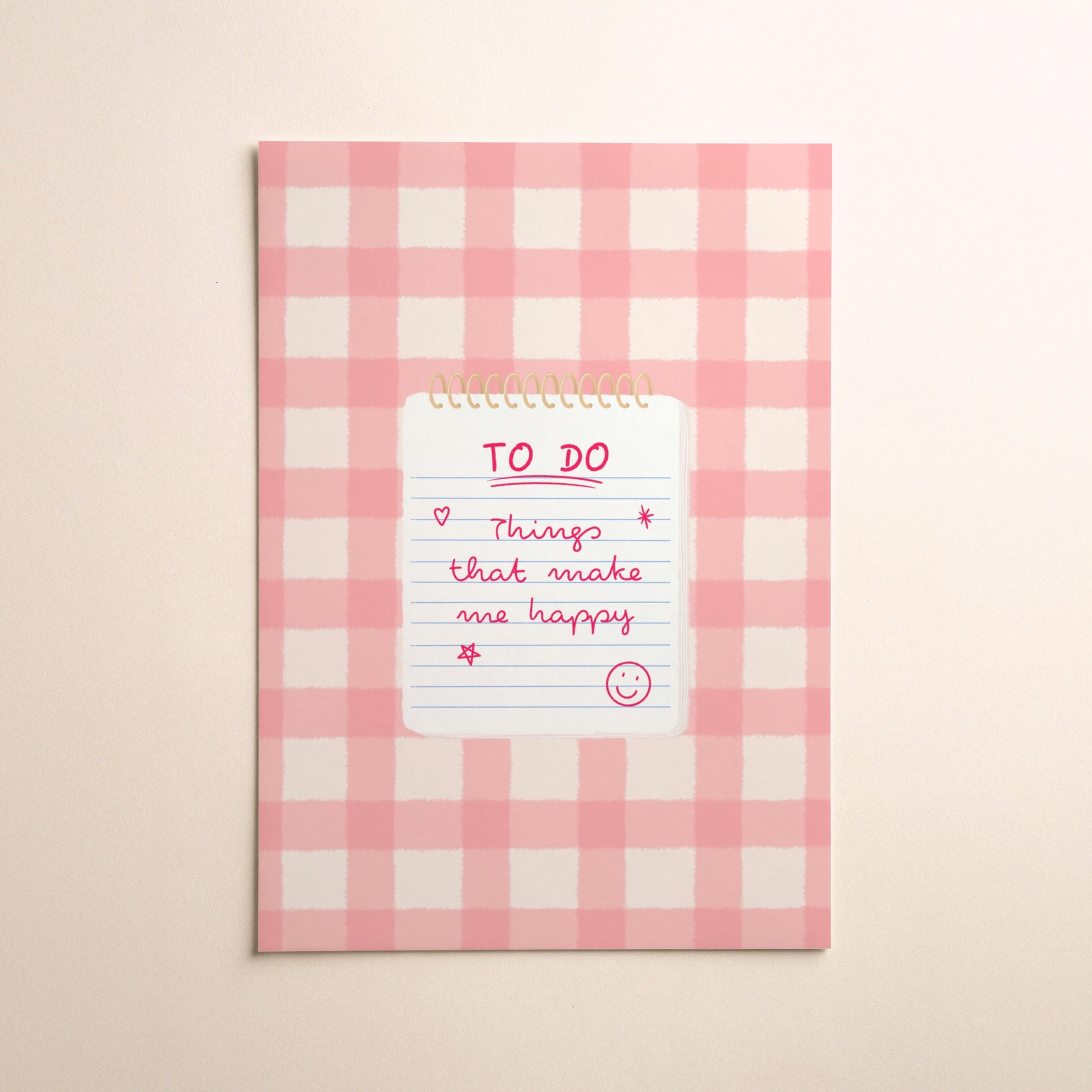 A pink and white gingham illustration print with a white notepad with gold spiral binding, featuring a pink handwritten 'TO DO' list that says ‘Things that make me happy’ with a smiley face, set against a warm beige background.