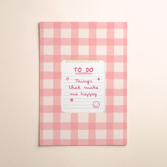 A pink and white gingham illustration print with a white notepad with gold spiral binding, featuring a pink handwritten 'TO DO' list that says ‘Things that make me happy’ with a smiley face, set against a warm beige background.