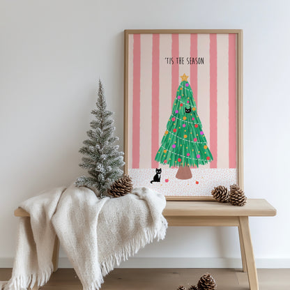 Framed Christmas-themed artwork on a wall with a small decorated tree and pinecones on a bench.