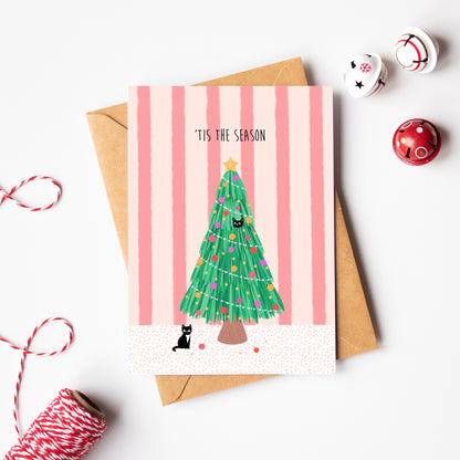 Christmas-themed greeting card with a tree and cat illustration on a pink striped background, surrounded by festive items.