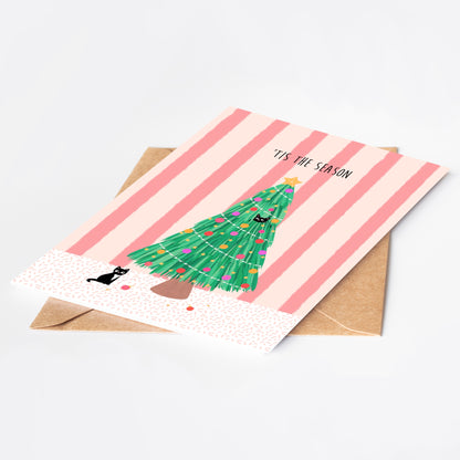 Greeting card with Christmas tree and cat illustration on pink striped background, with a brown kraft envelope