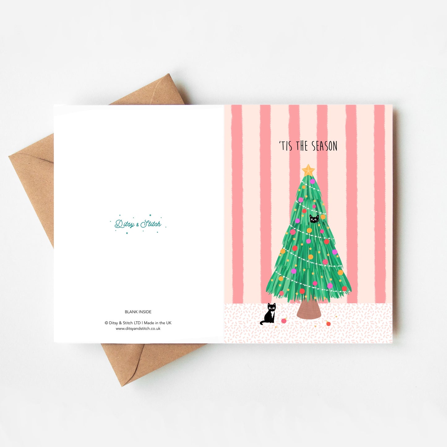 Christmas card with a tree and cats design on a pink striped background, with a brown kraft envelope