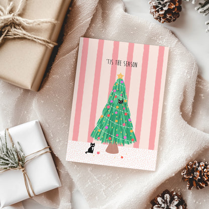 Christmas card with a tree and cat design on a striped background, surrounded by wrapped gifts and pine cones.