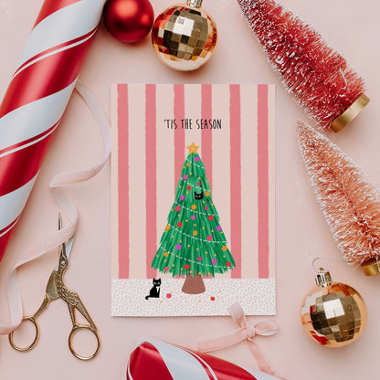 Christmas-themed card with a tree and cat illustration, surrounded by festive decorations on a pink background.
