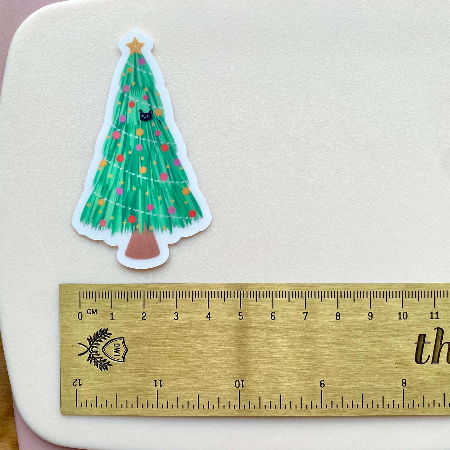 Sticker of a Christmas tree with cats on a white surface next to a ruler for scale.