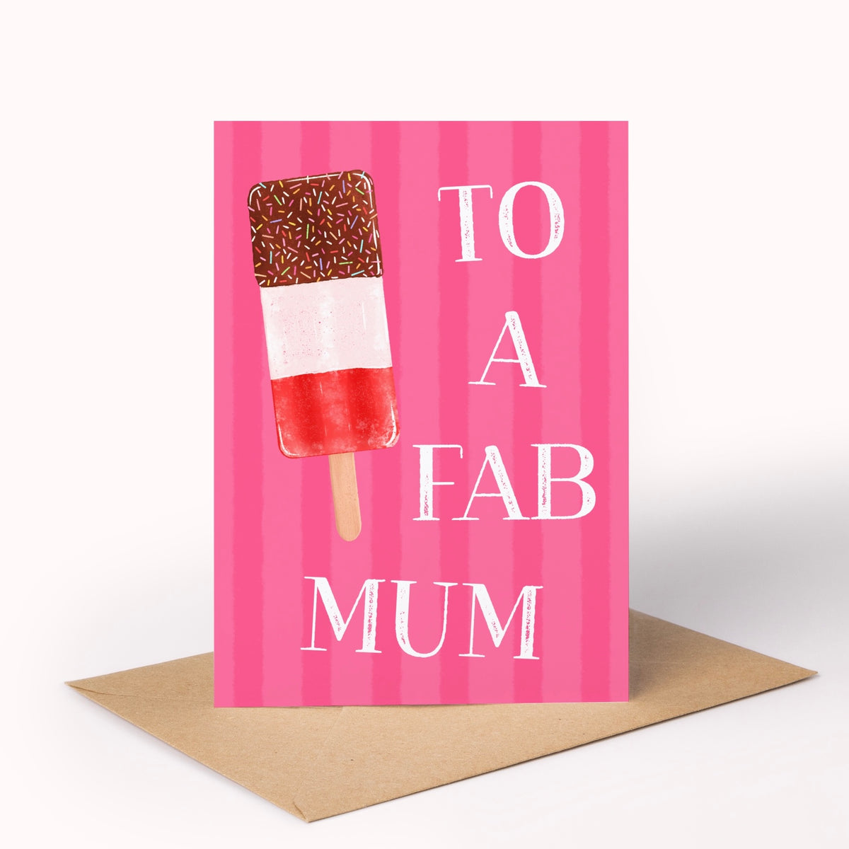 A greeting card with a pink striped background, featuring an illustration of a chocolate-dipped ice lolly and the text 'TO A FAB MUM' in white. The card is displayed upright on a brown kraft envelope against a clean white background.