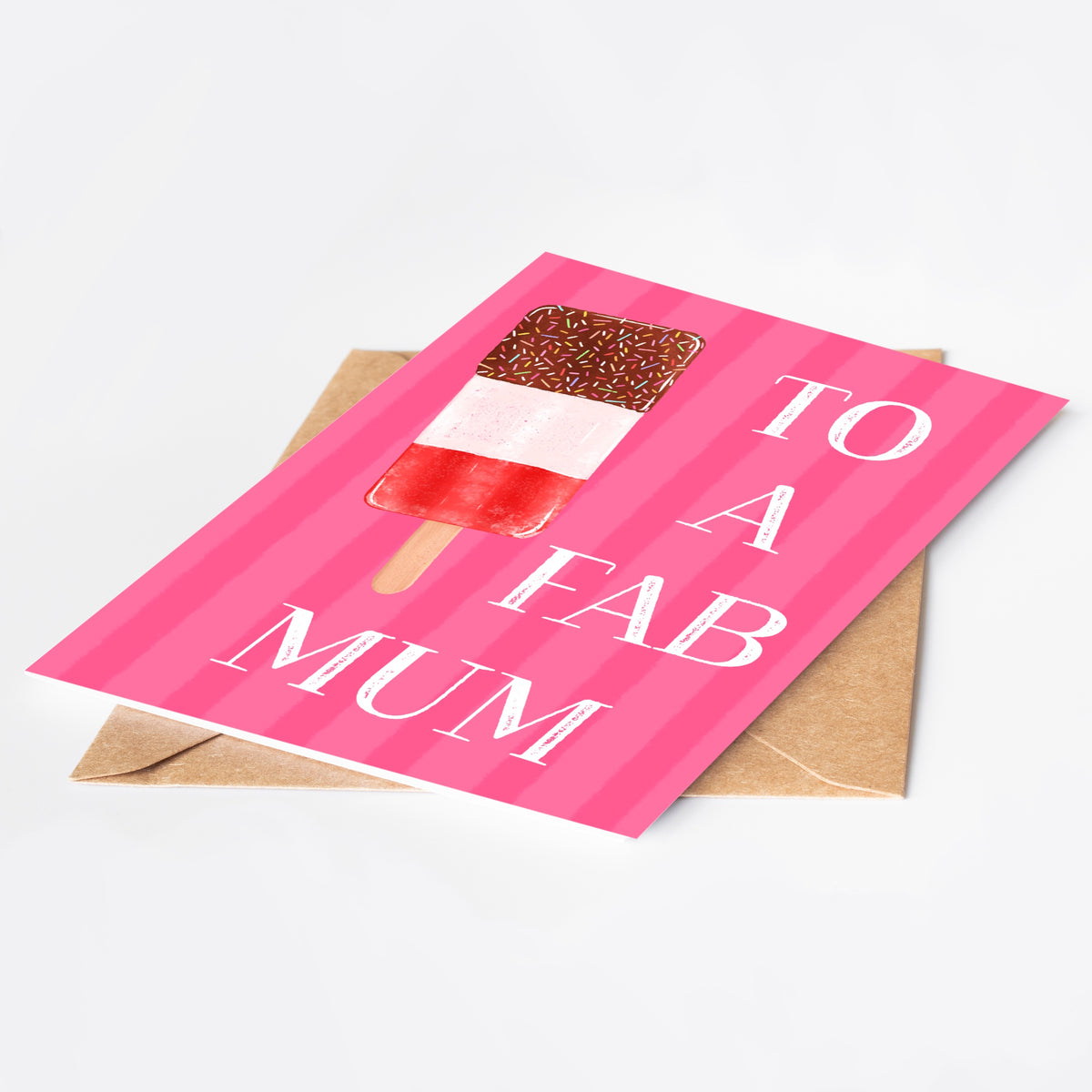 A pink striped greeting card with an ice lolly illustration and the words 'TO A FAB MUM' in white, shown on top of a brown envelope against a light grey background.