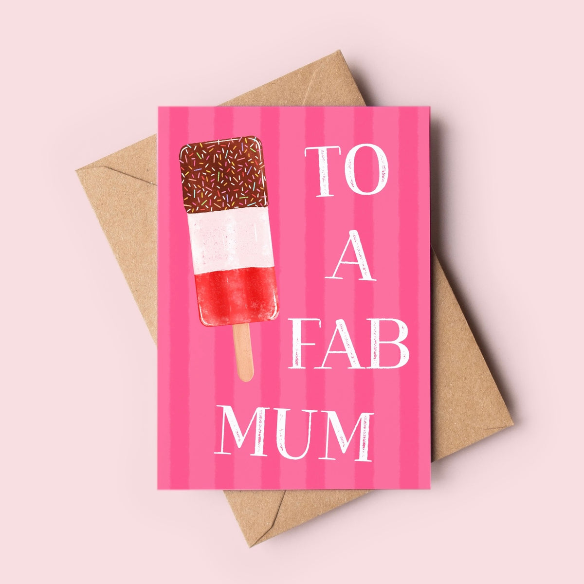 A pink greeting card with vertical stripes and a hand-drawn ice lolly illustration, printed with the words 'TO A FAB MUM' in white. The card is shown with a brown kraft envelope on a light pink background.