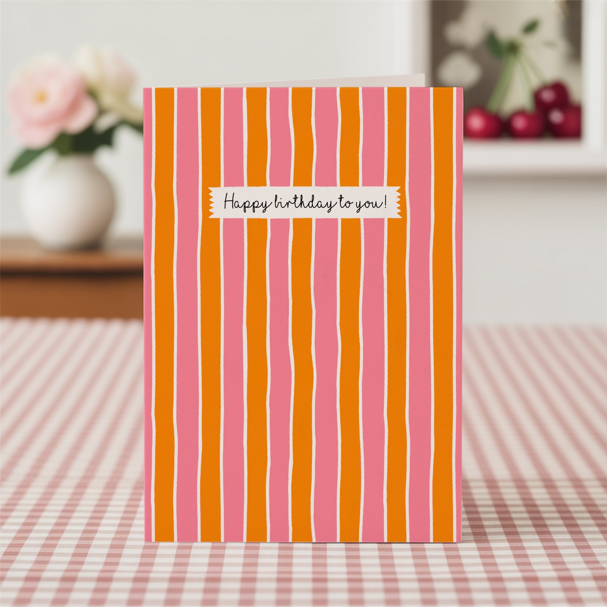 Striped birthday card with pink and orange vertical stripes on a checkered tablecloth.