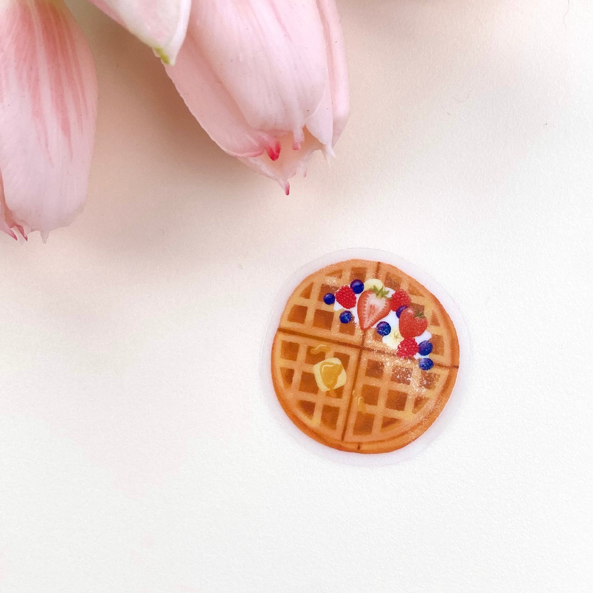 A transparent sticker with a detailed illustration of some breakfast waffles with syrup, butter and mixed summer berries