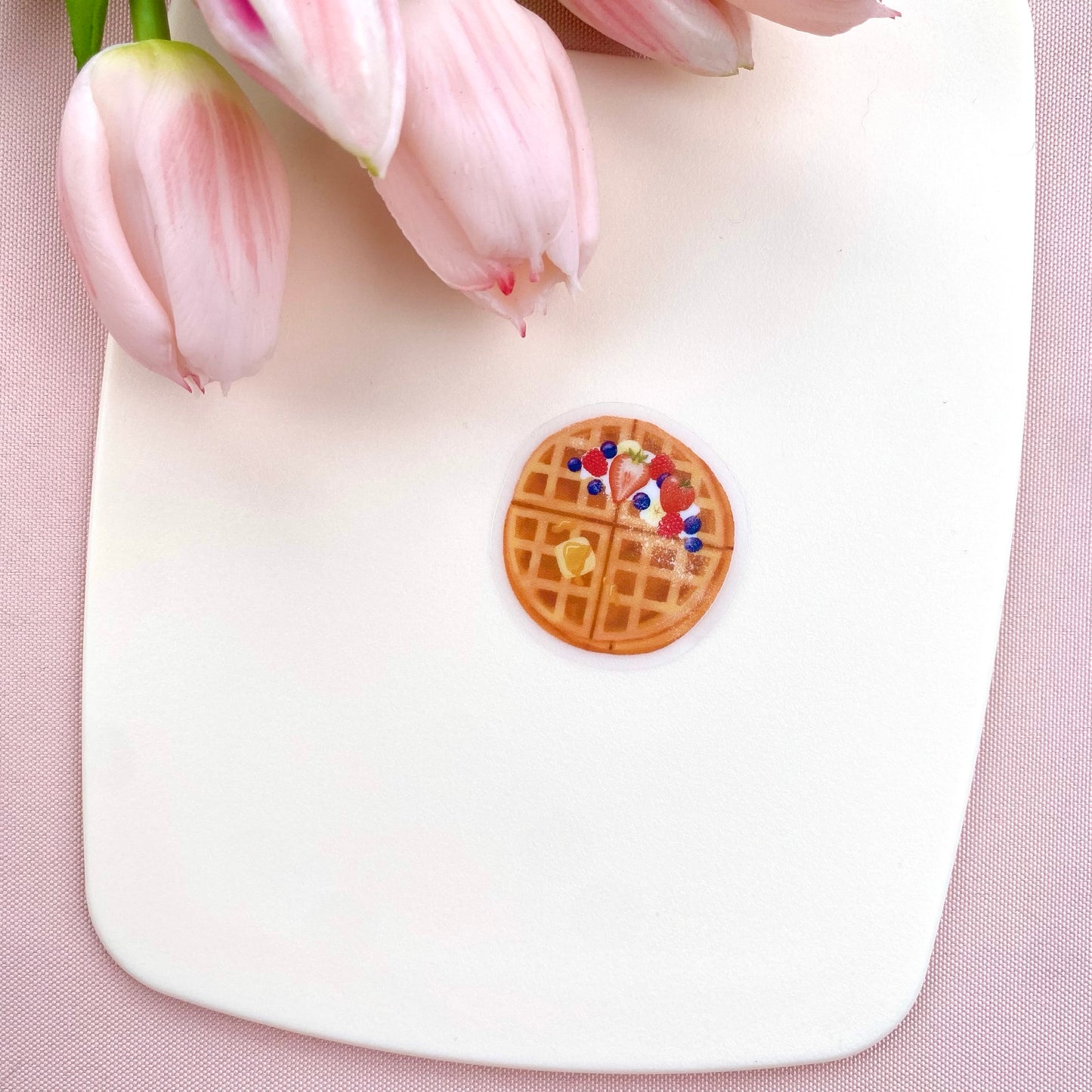 A transparent sticker with a detailed illustration of some breakfast waffles with syrup, butter and mixed summer berries