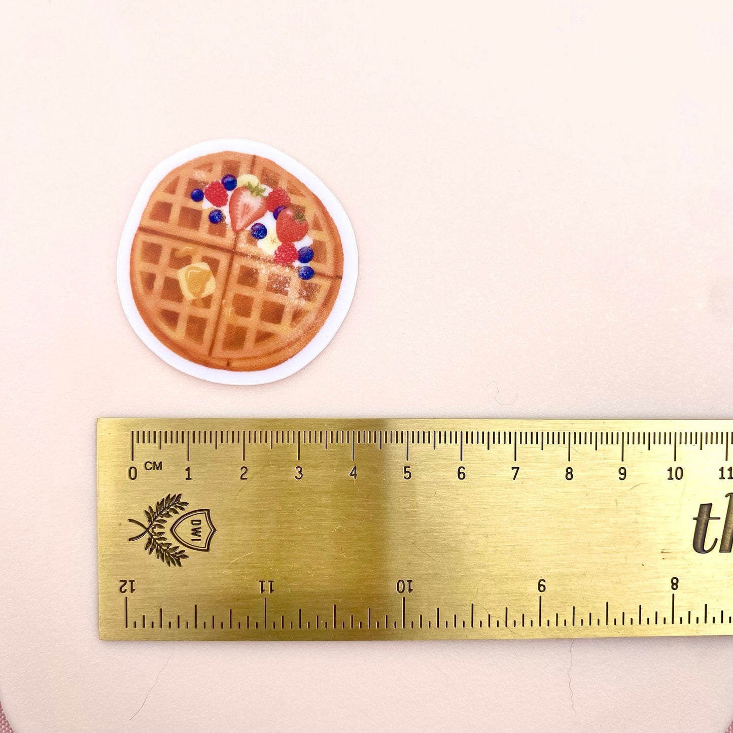 A transparent sticker with a detailed illustration of some breakfast waffles with syrup, butter and mixed summer berries. Shown with a ruler for size reference.