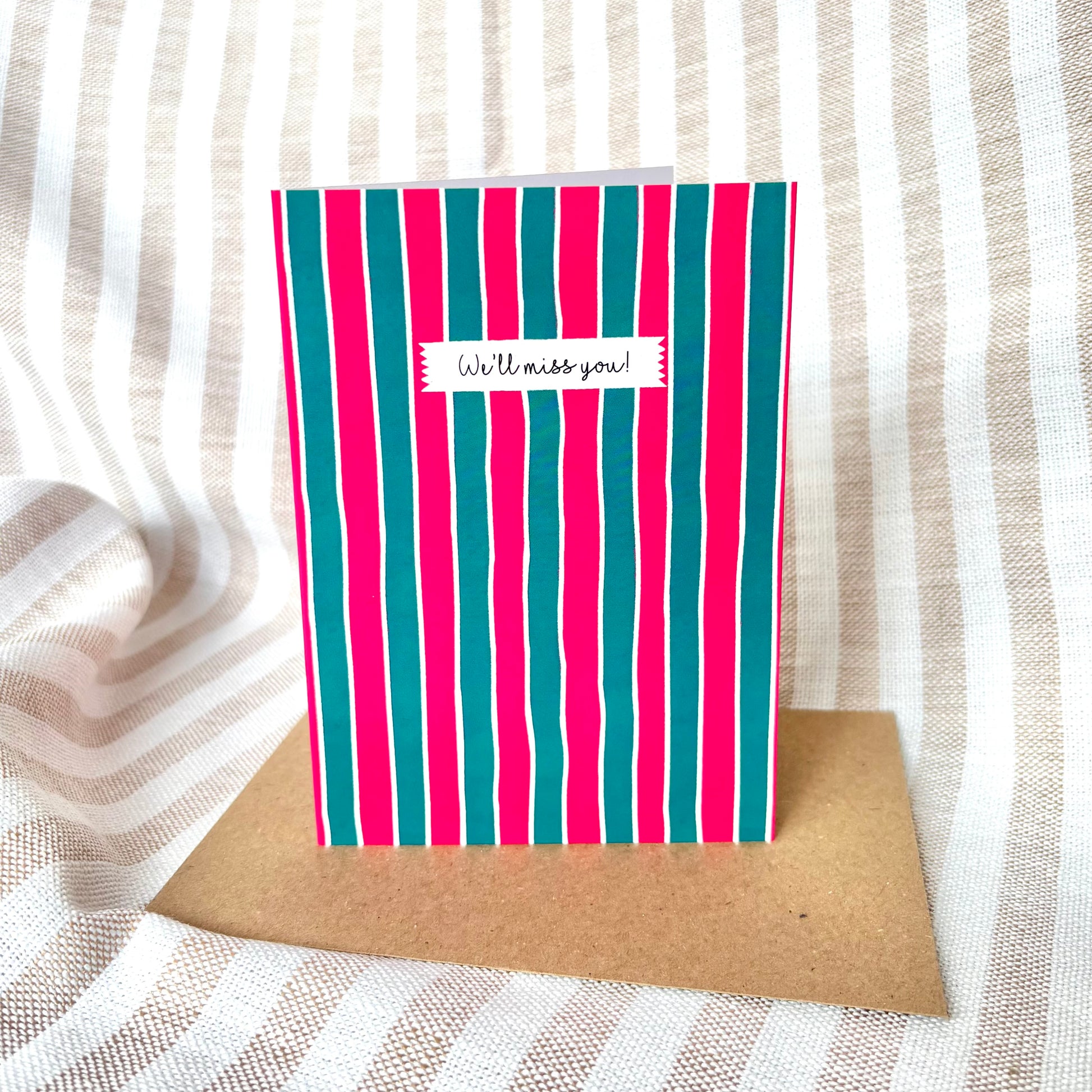 Striped card with 'We'll miss you!' message on a textured fabric background