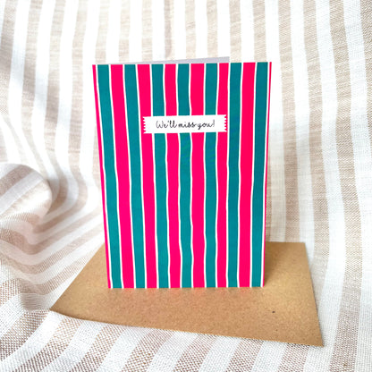 Striped card with 'We'll miss you!' message on a textured fabric background