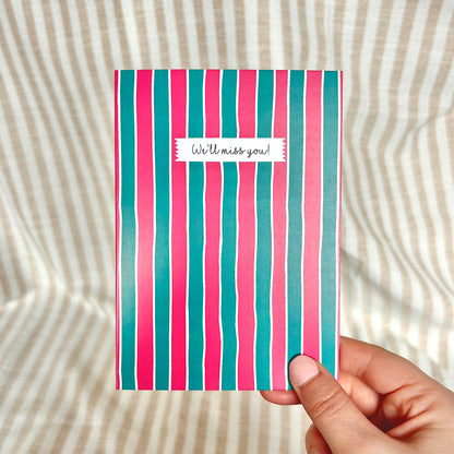 Striped card with 'We'll miss you!' message held by a hand on a textured background