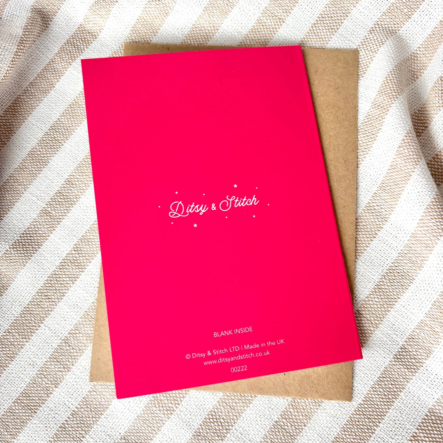 Pink card with 'Ditsy & Stitch' branding on the back, with a brown kraft envelope on a beige fabric background