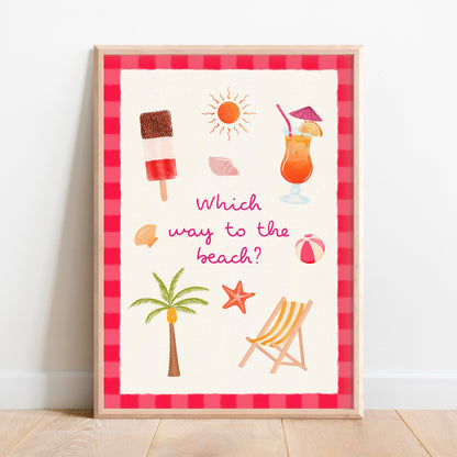 A framed summer-themed art print leaning against a white wall on a light wood floor. The print features a red and pink striped border, a cream textured background, and illustrations of beach items including a palm tree, deck chair, fab ice lolly, cocktail, sun, starfish, and beach ball, with the text 'Which way to the beach?'.