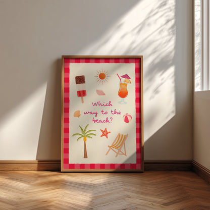 A framed beach-themed art print leaning against a wall on a wooden floor. The print features a pink and red striped border and colourful illustrations of a cocktail, palm tree, beach chair, starfish, and sun with the text 'Which way to the beach?'.