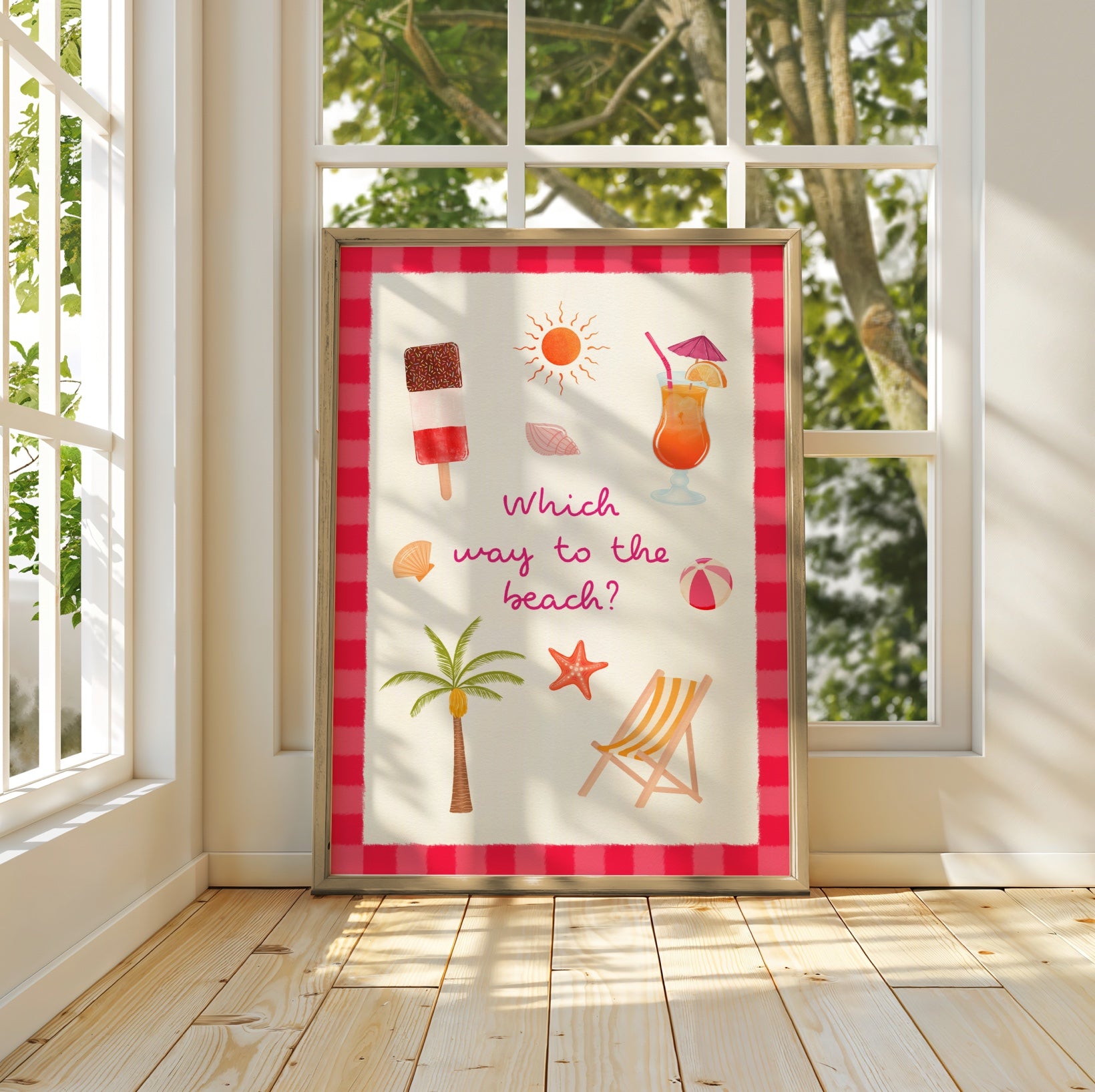 A framed summer-themed art print leaning against a window in a sunlit room. The print features beach and poolside illustrations including a popsicle, cocktail, palm tree, starfish, beach chair, seashells, and a sun, with the text 'Which way to the beach?'.