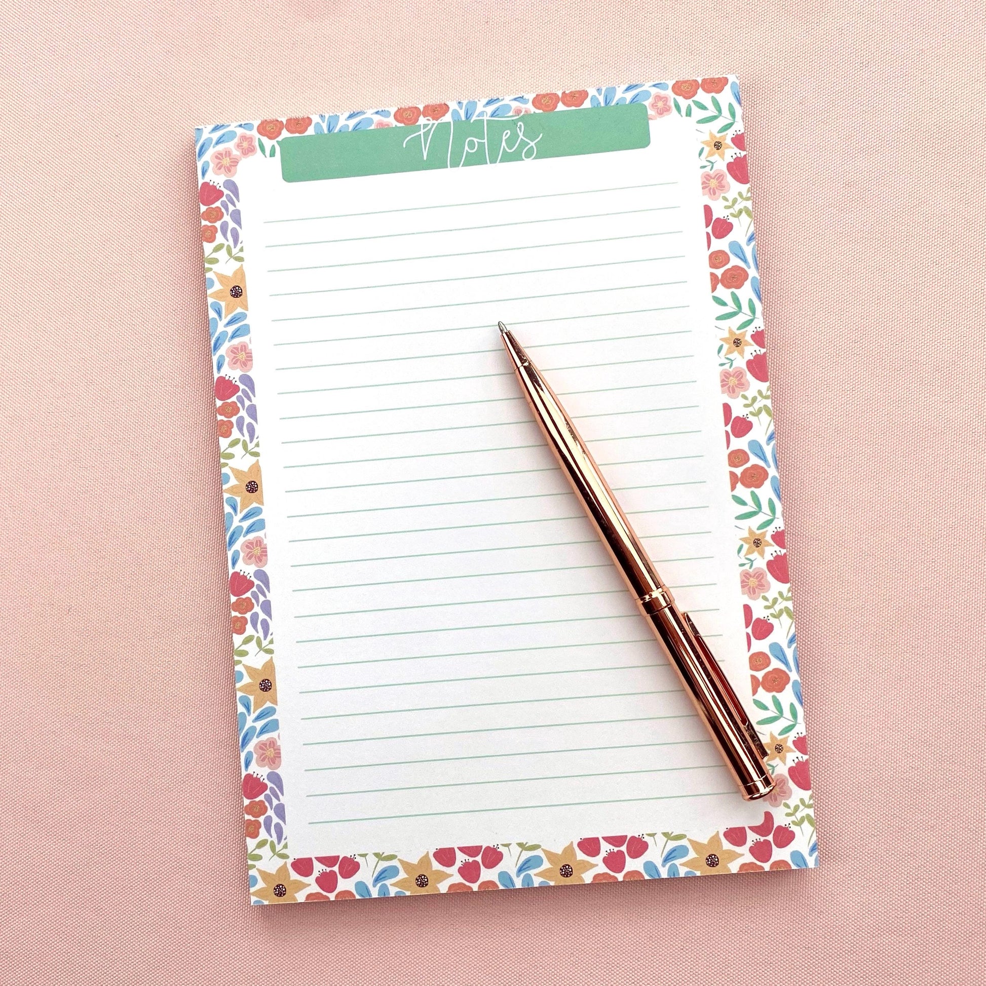 Floral-patterned notepad with a pen on a pink background