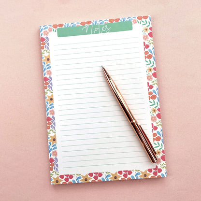Floral-patterned notepad with a pen on a pink background