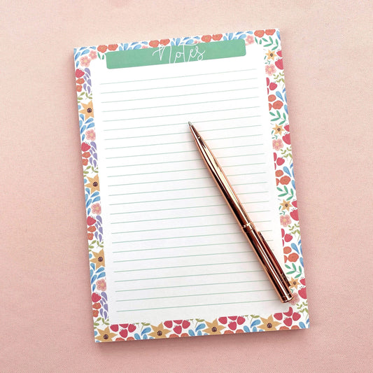 Floral-patterned notepad with a pen on a pink background