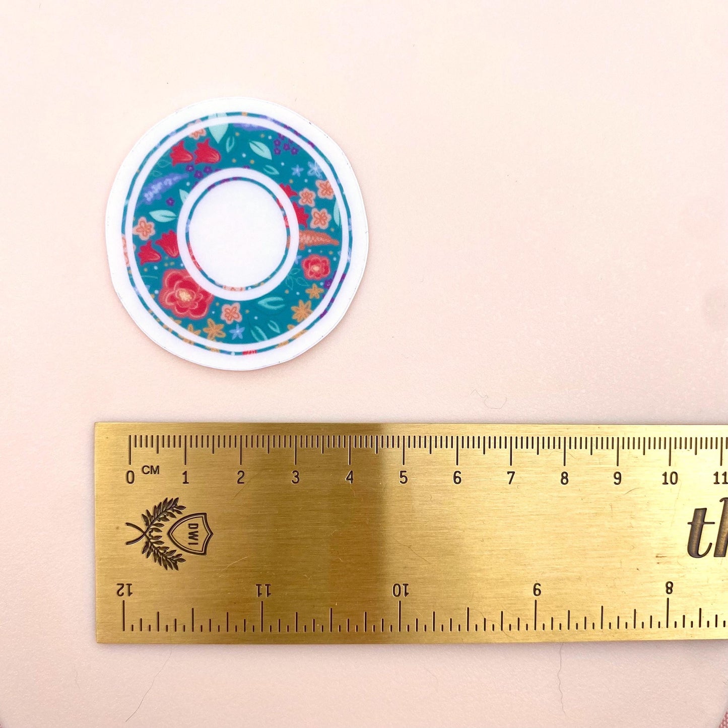 Letter 'O' floral sticker on a beige background with a ruler for scale.