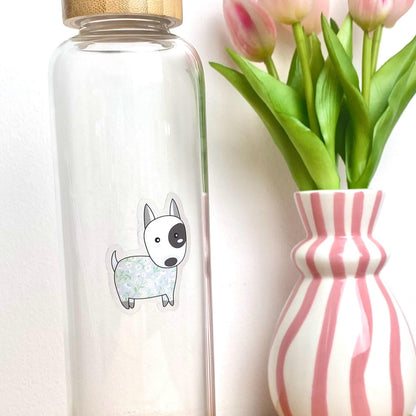 Clear glass bottle with a dog sticker next to a striped vase with tulips on a white background
