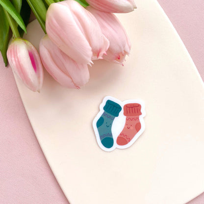 A sticker of two cartoon socks on a pink surface with pink tulips in the background