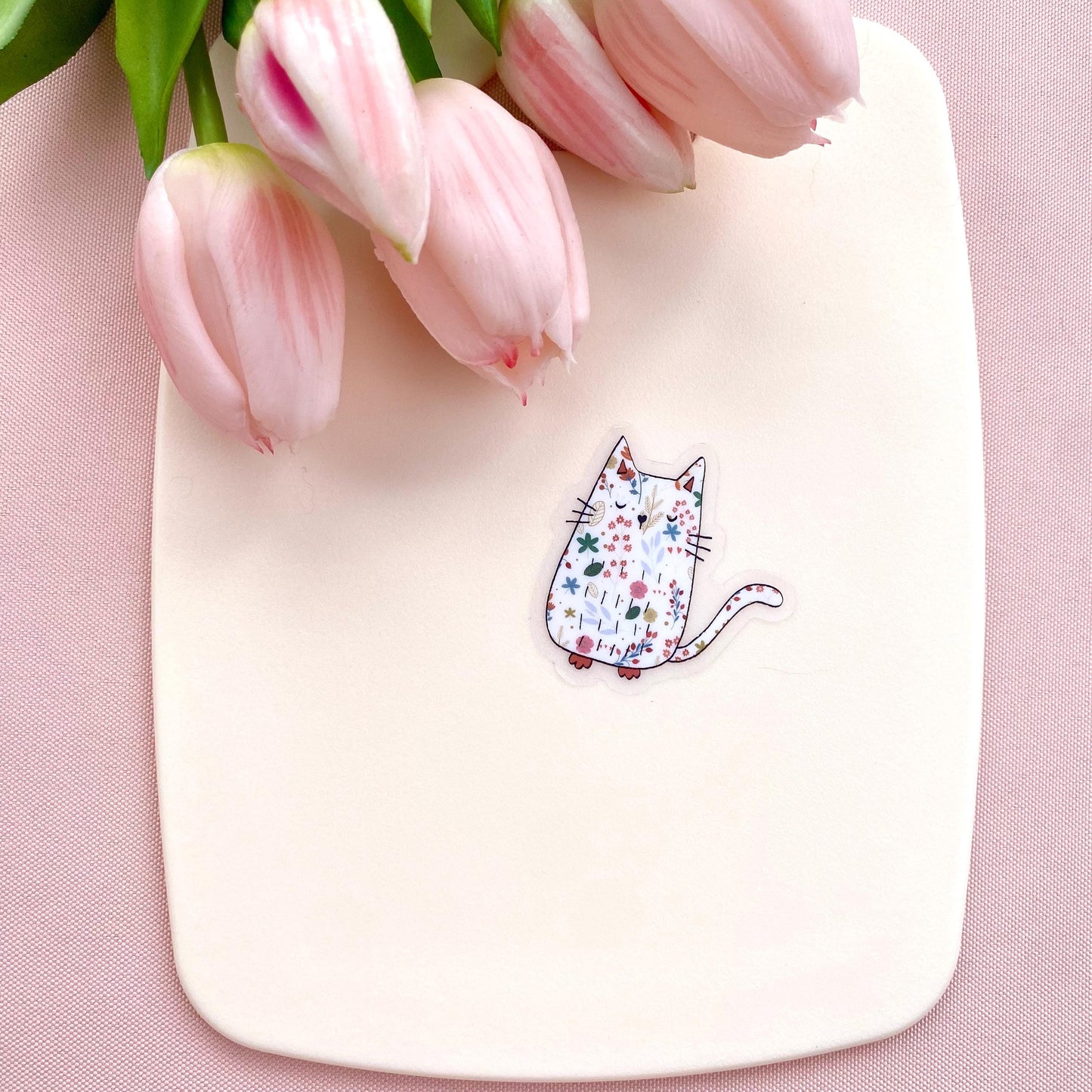White board with a cat illustration sticker and pink tulips on a pink background