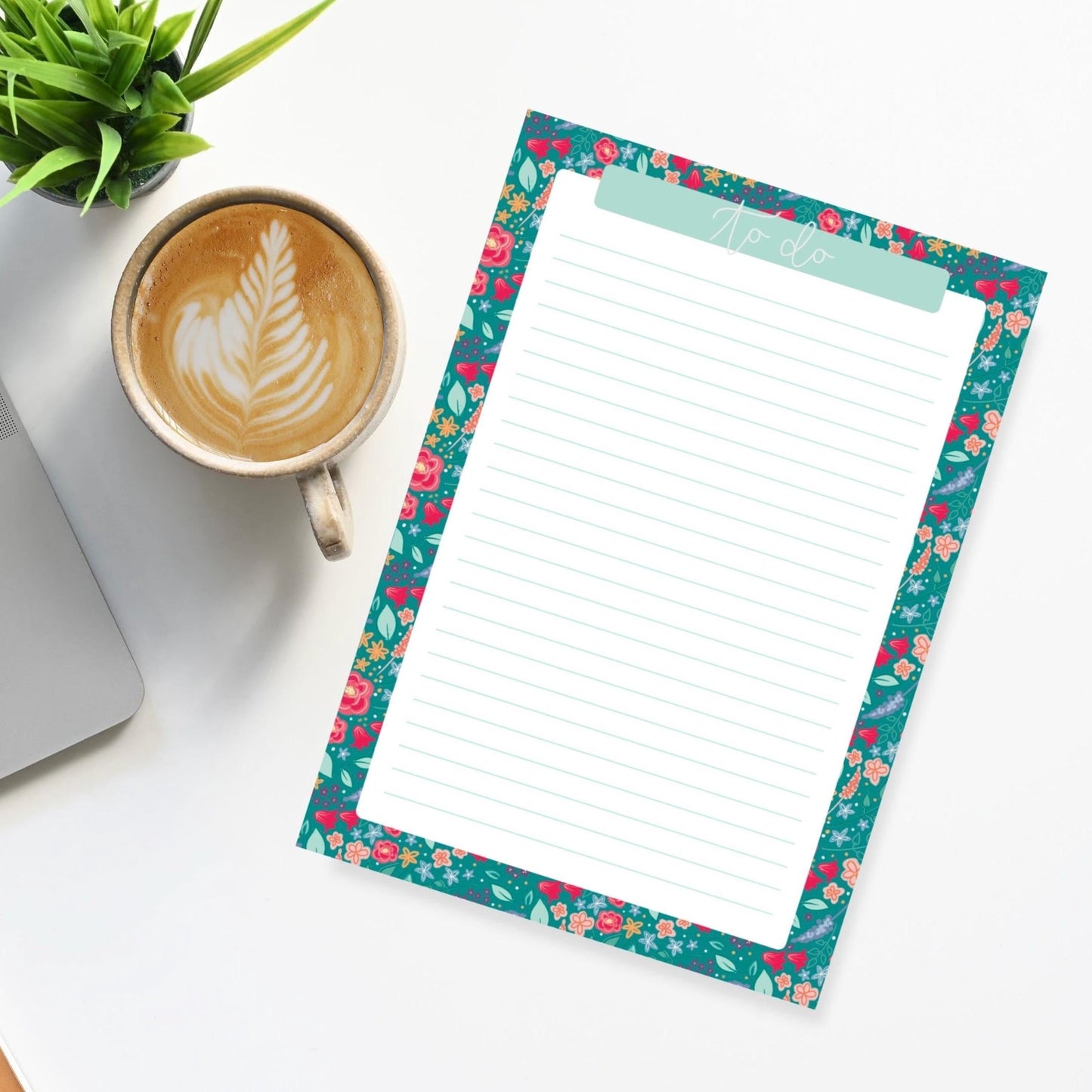 Floral border notepad with a cup of coffee and laptop on a white surface