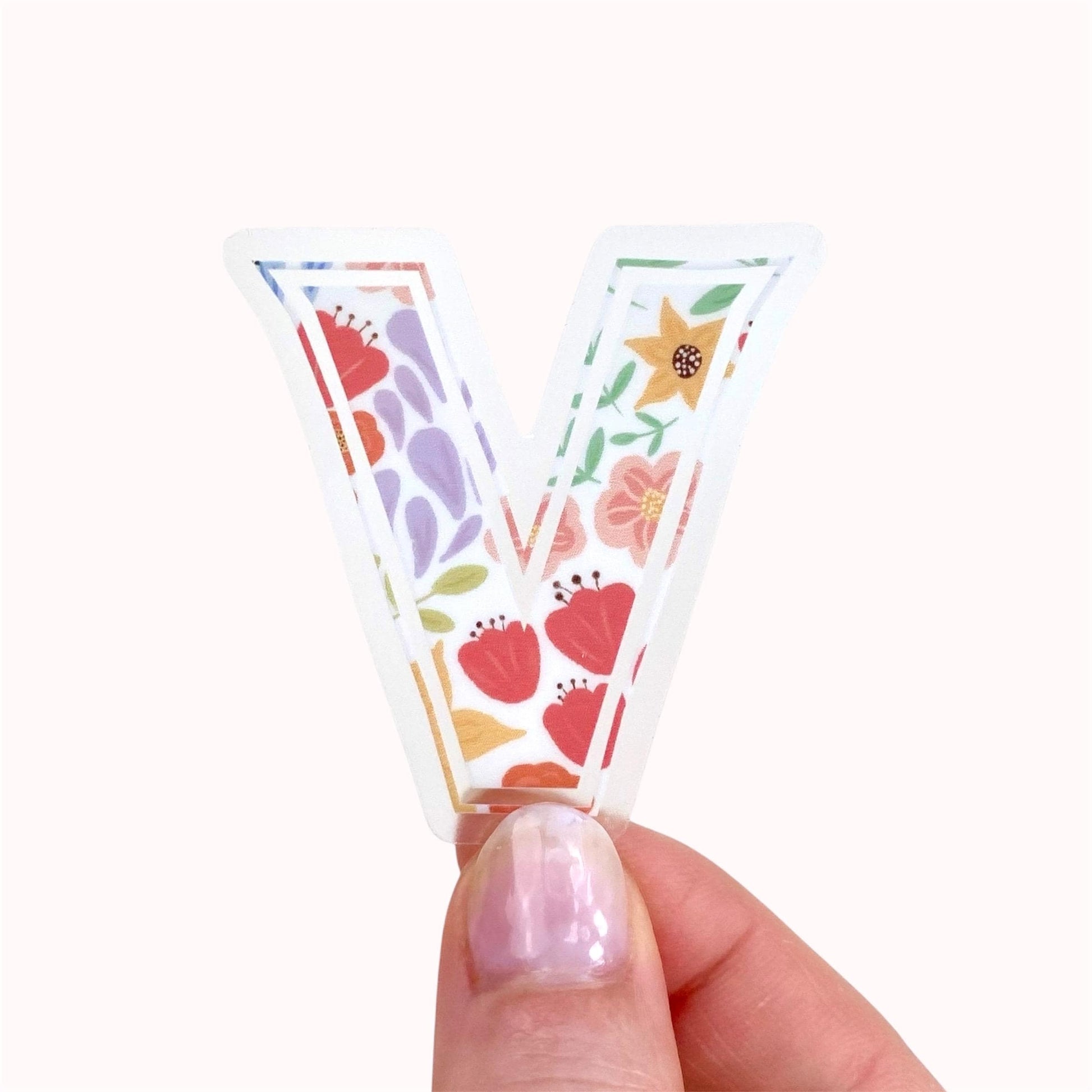 Hand holding a floral letter 'V' sticker against a white background