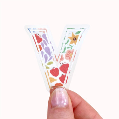 Hand holding a floral letter 'V' sticker against a white background