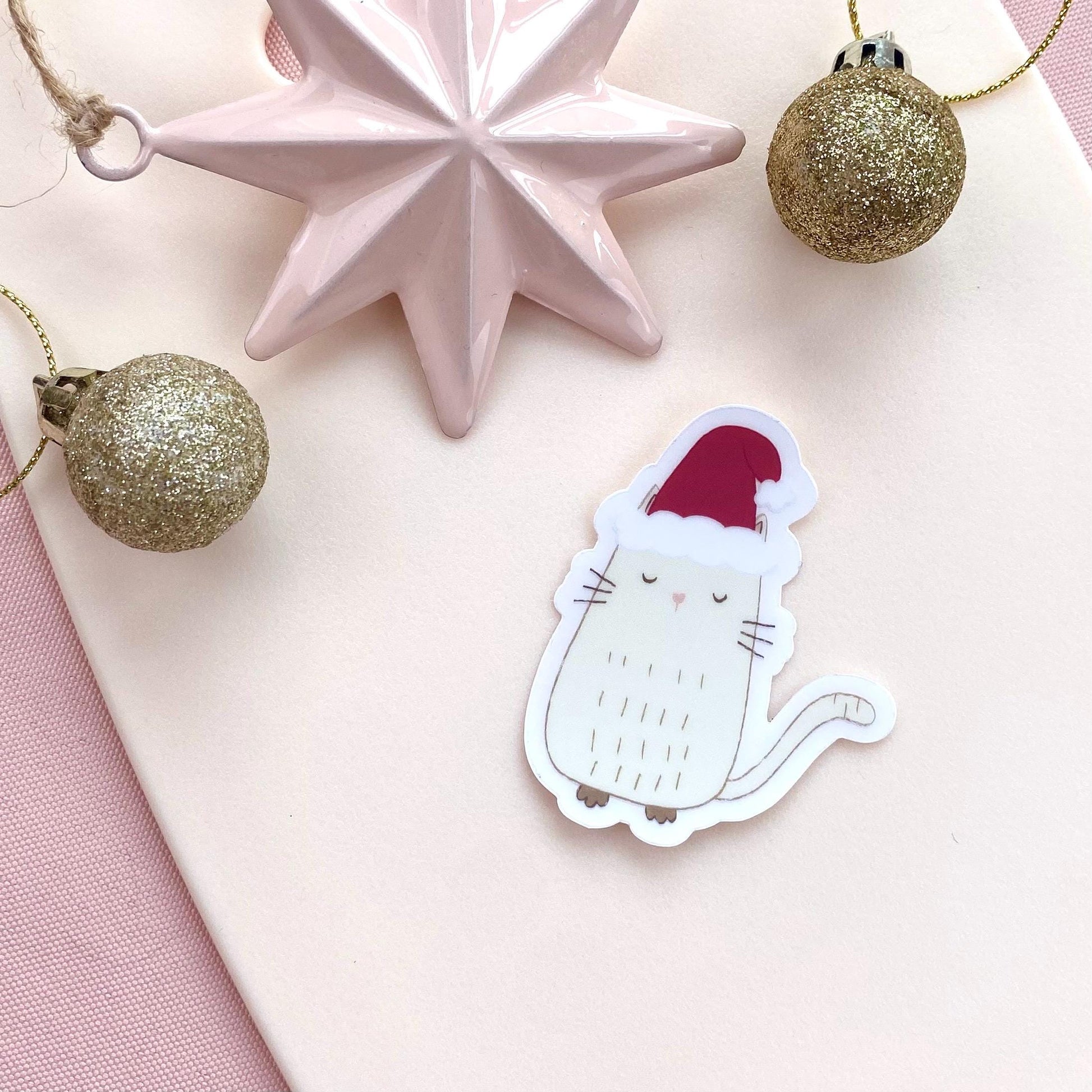 Sticker of a cat in a Santa hat with Christmas decorations on a pink surface