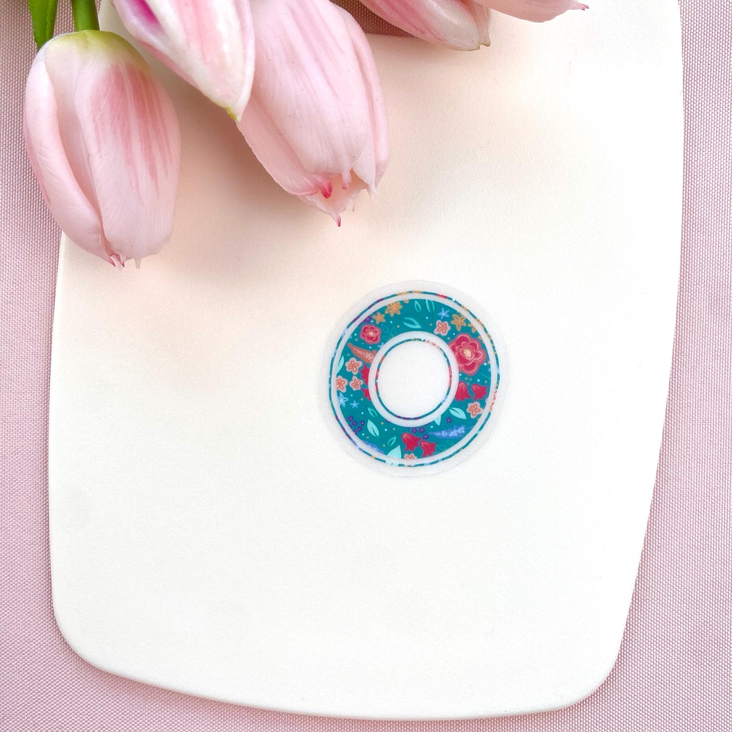 Decorative letter 'O' sticker with floral pattern held on a white background with pink tulips