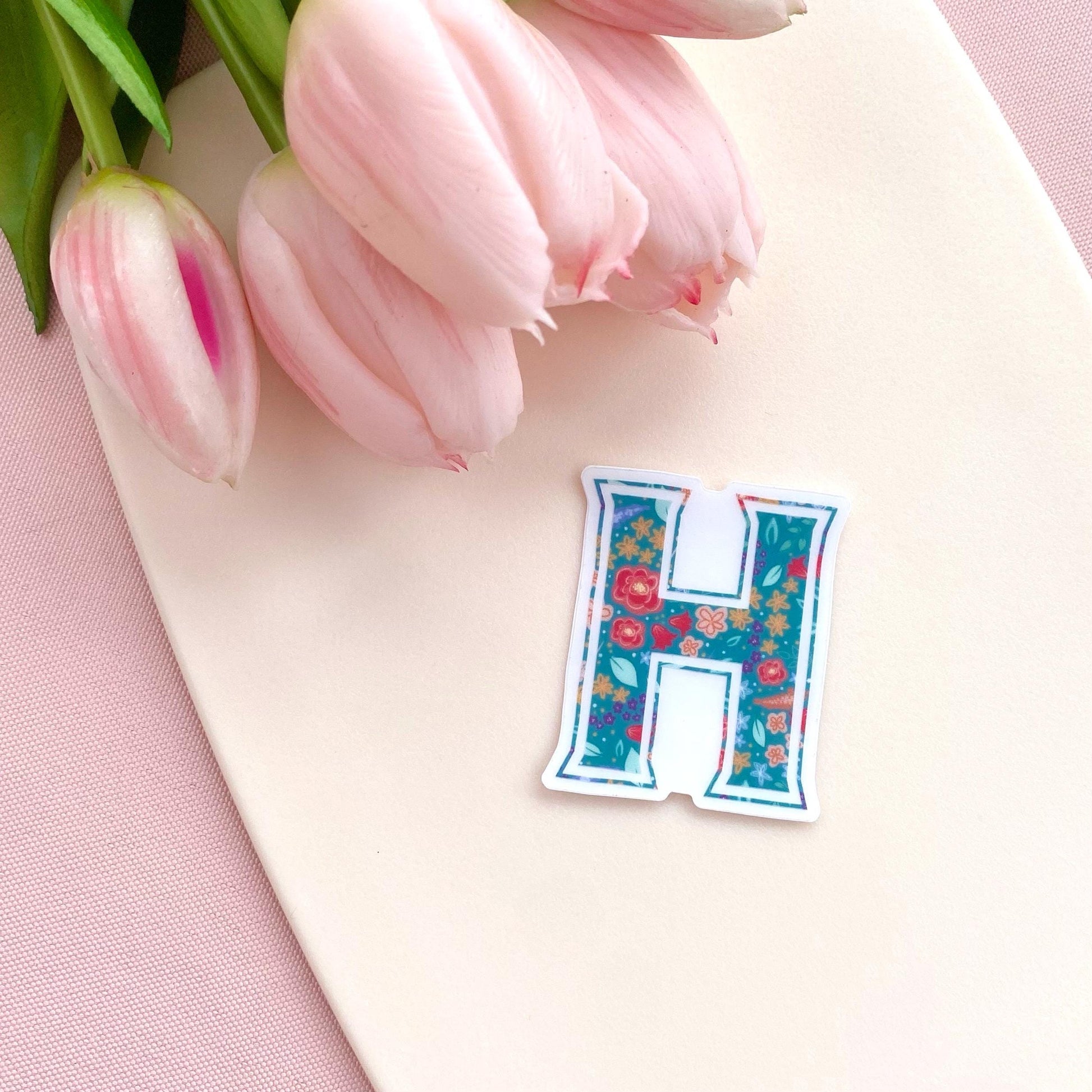 Floral letter 'H' sticker on a pink surface with pink tulips