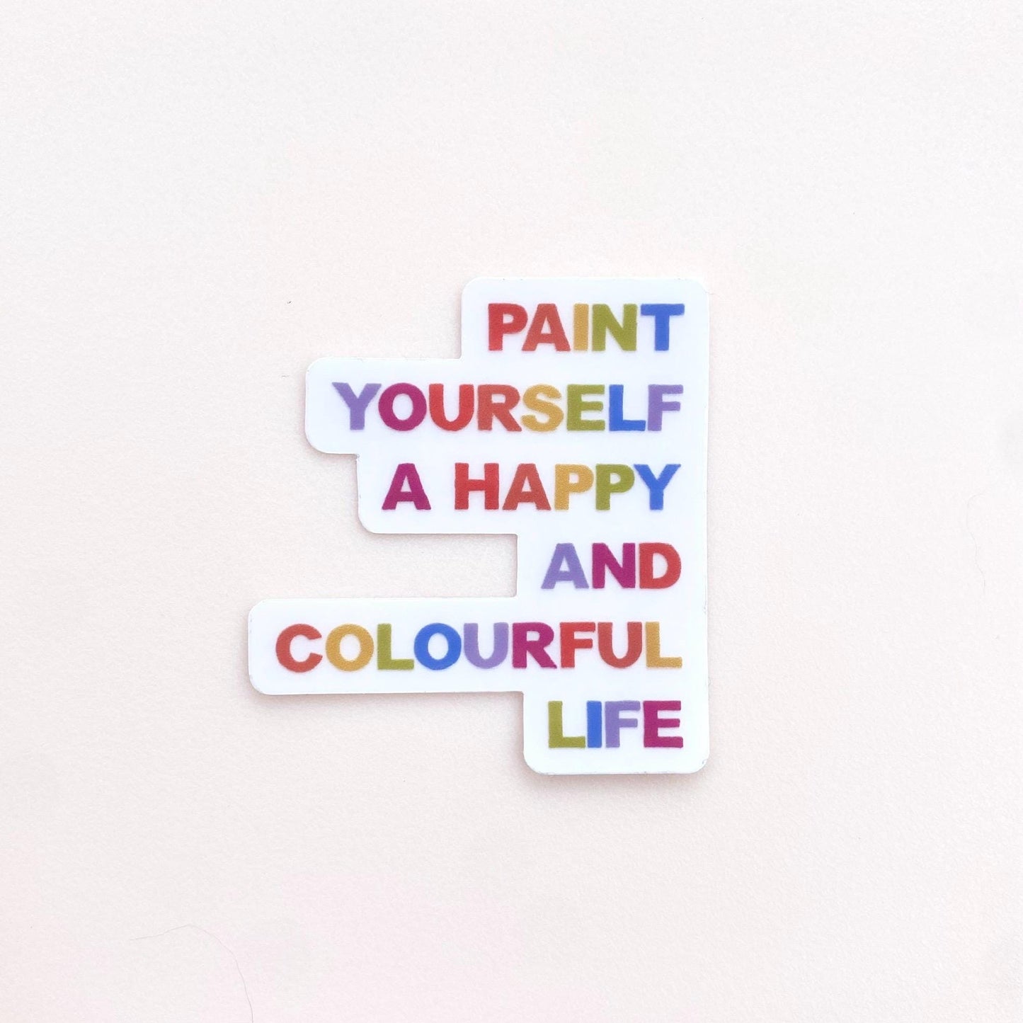 A clear sticker with motivational quote 'Paint yourself a happy and colourful life' on a white background