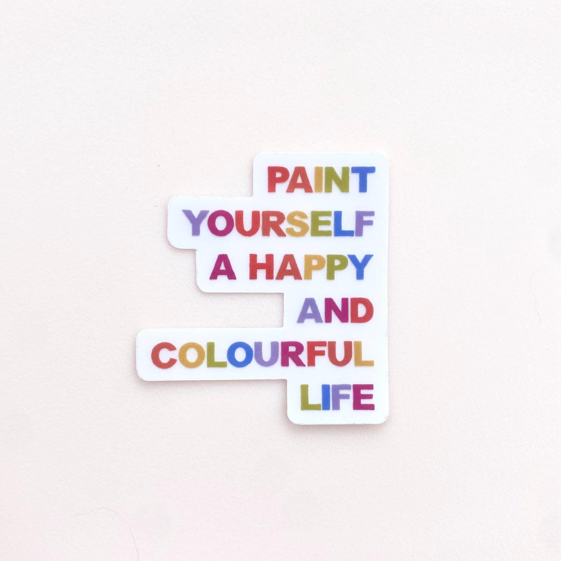 A clear sticker with motivational quote 'Paint yourself a happy and colourful life' on a white background