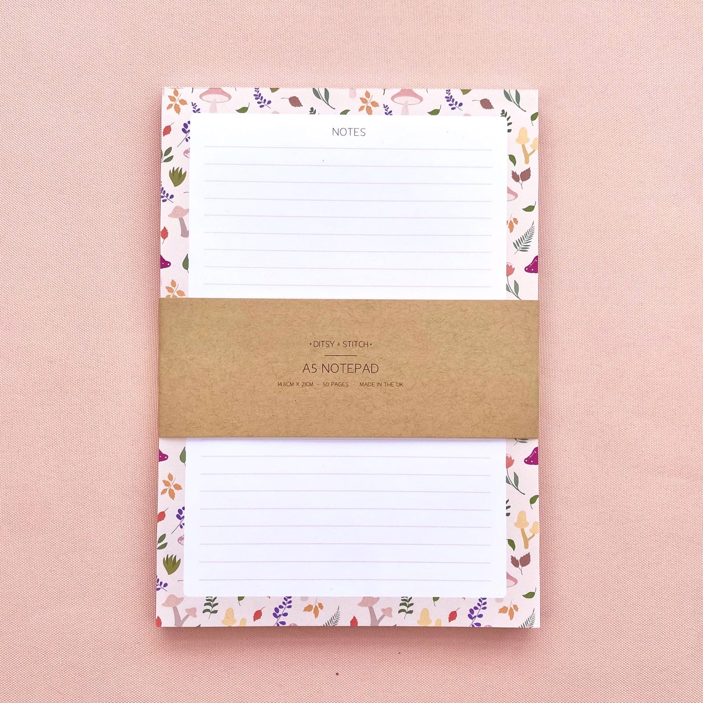 A lined notepad on a pink background, with a beige border patterned with autumn leaves and mushrooms