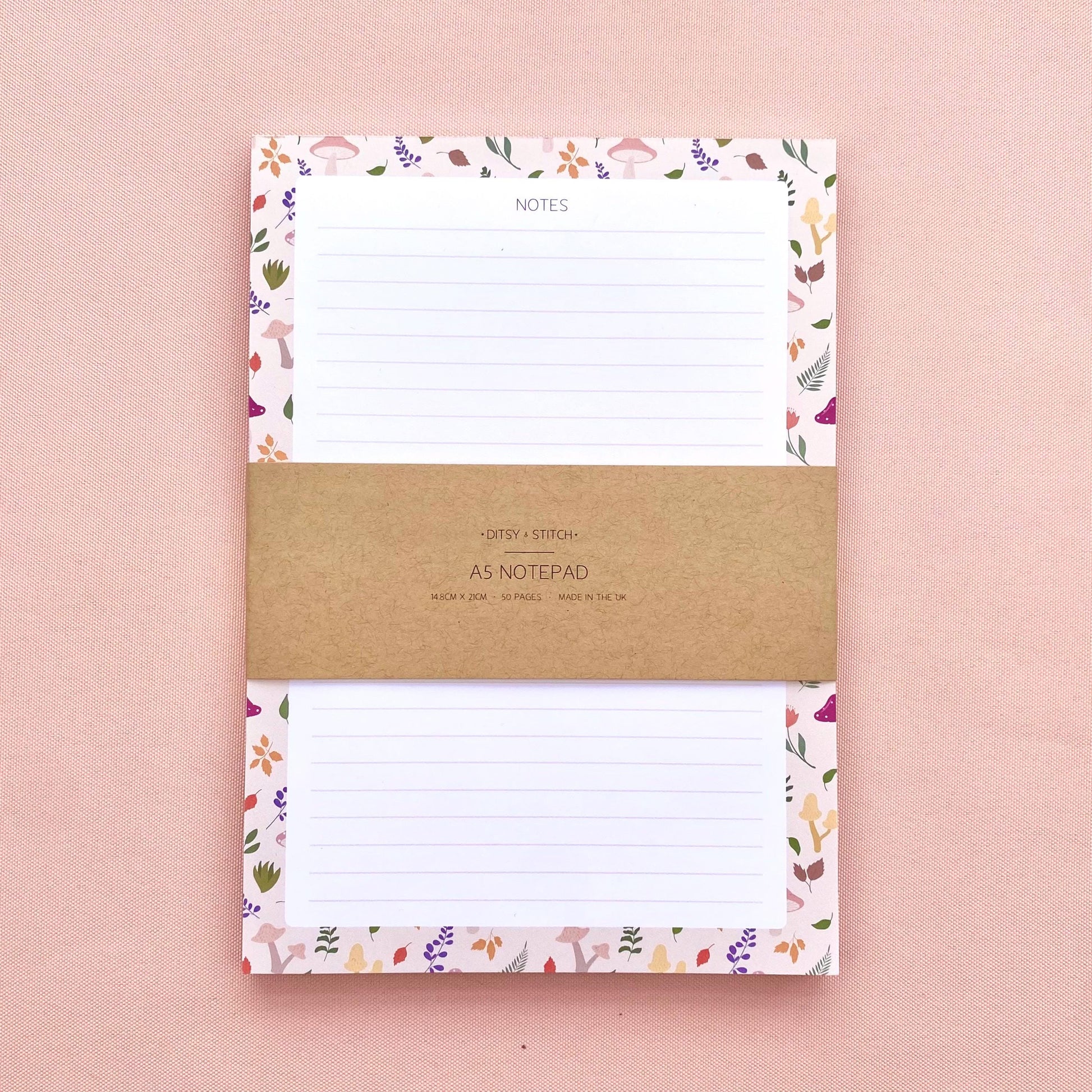 A lined notepad on a pink background, with a beige border patterned with autumn leaves and mushrooms