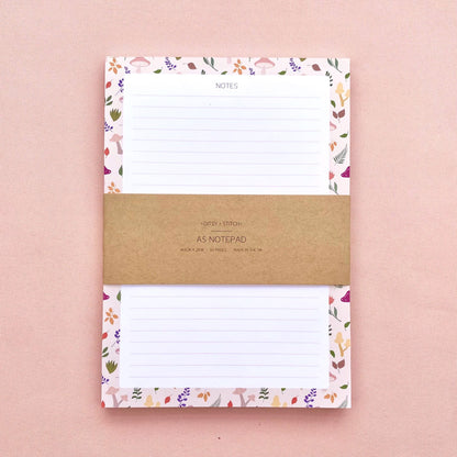 A lined notepad on a pink background, with a beige border patterned with autumn leaves and mushrooms