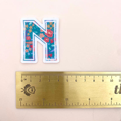 Floral letter 'N' sticker next to a ruler on a beige background