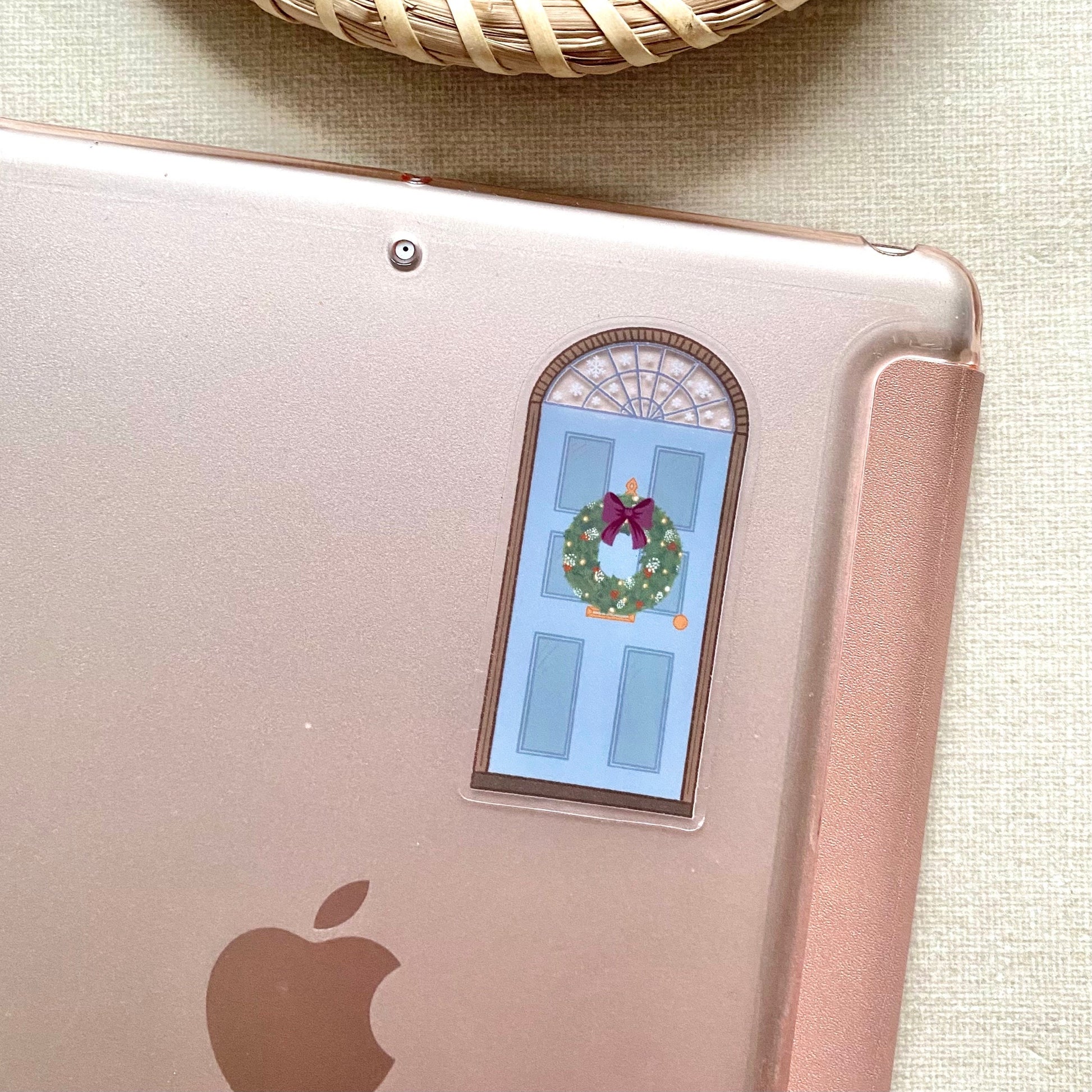 A sticker with a blue door decorated for Christmas shown stuck to the back of a pink ipad.