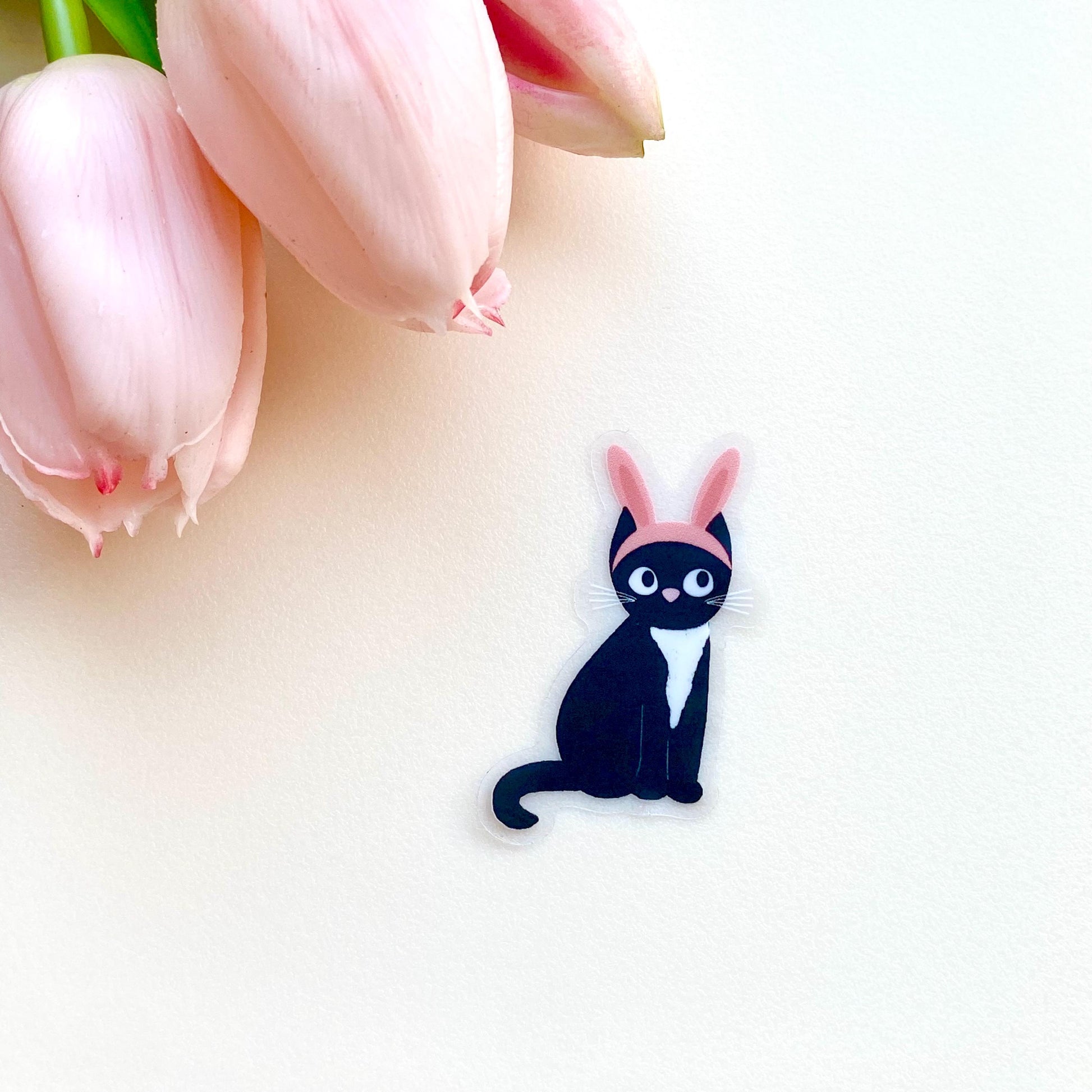 Sticker of a black cat with pink bunny ears on a white surface.