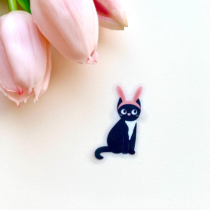 Sticker of a black cat with pink bunny ears on a white surface.