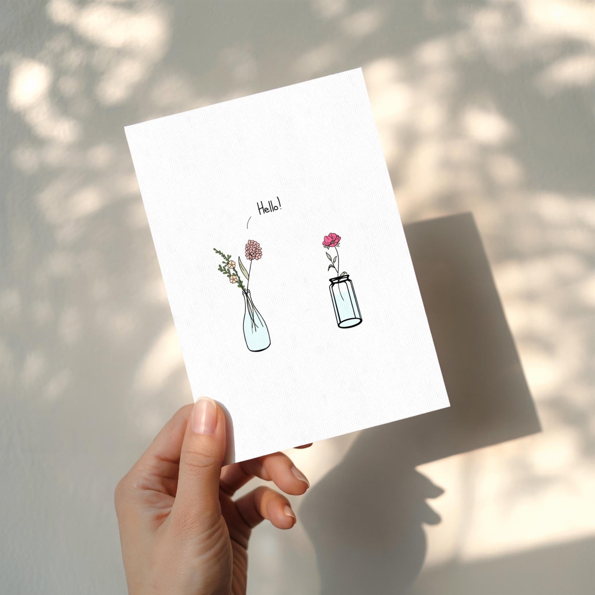 Hand holding a card with illustrations of vases and flowers on a light background