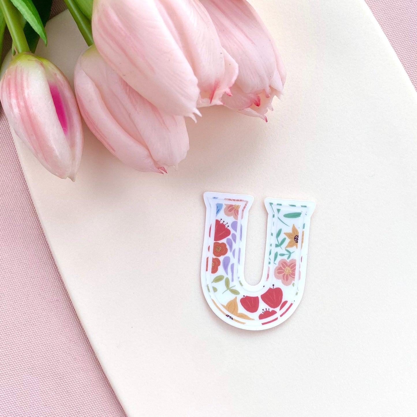 Floral letter 'U' sticker on a white surface with pink tulips in the background