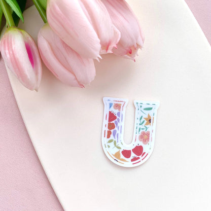 Floral letter 'U' sticker on a white surface with pink tulips in the background