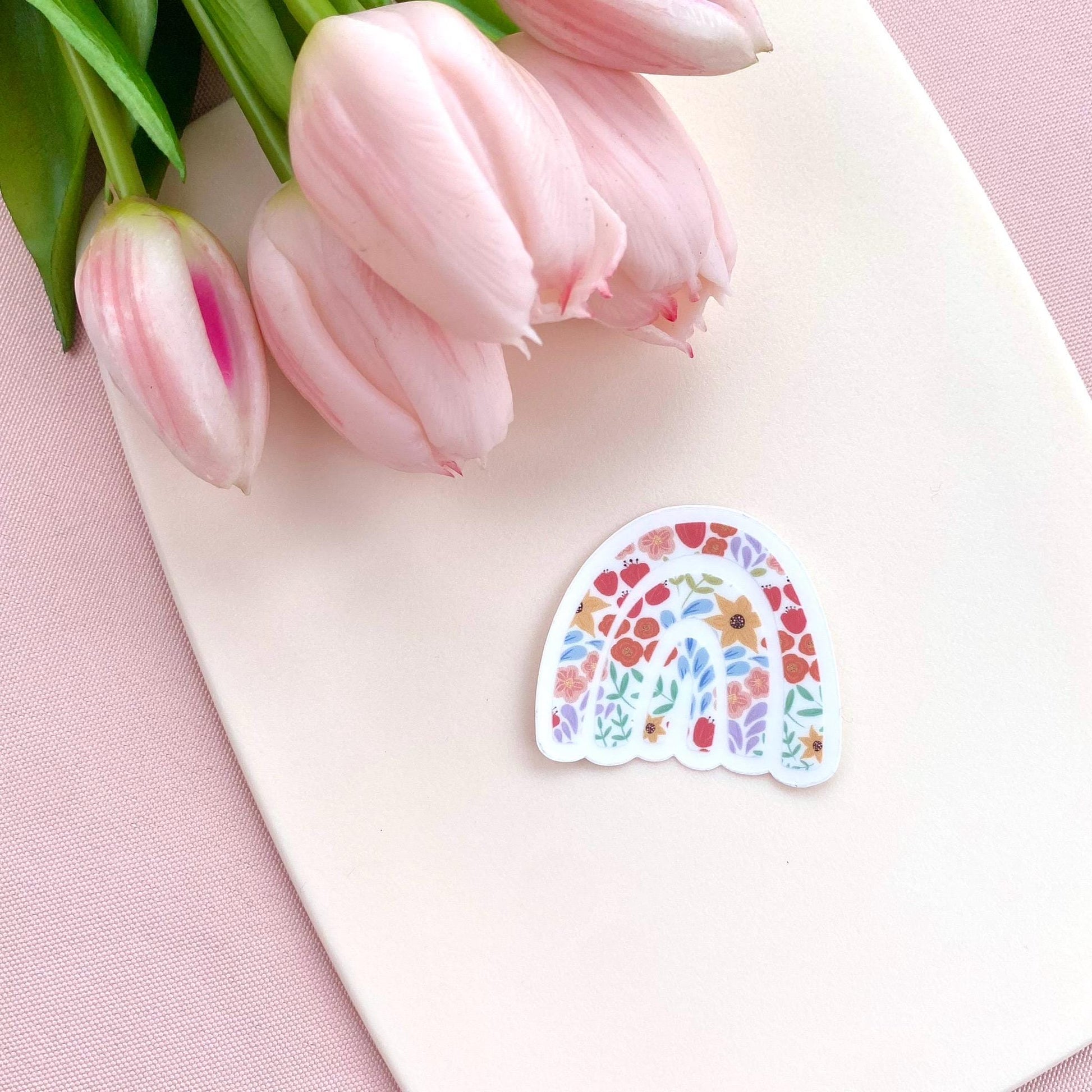 Colourful rainbow sticker with floral pattern against a cream background with pink tulips.